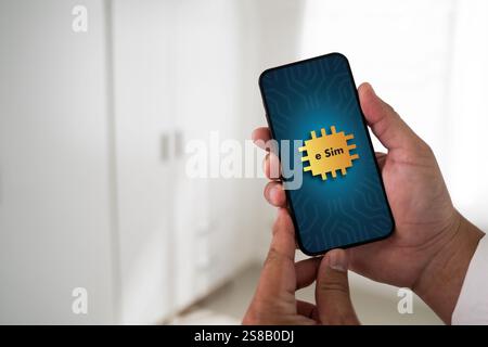 A person is holding a cell phone with a gold sticker on it that says "E-SIM". The person is likely checking their phone or using it for some purpose Stock Photo