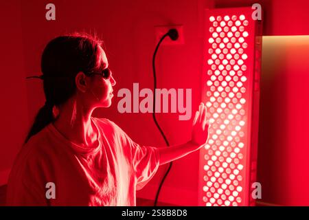 Close-up view of a young woman using red light therapy equipment indoors Stock Photo