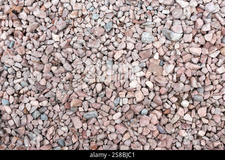 A texture-rich close-up of small, rough gravel stones in shades of pink, gray, and beige. The natural uneven surface and dispersed colors provide an o Stock Photo