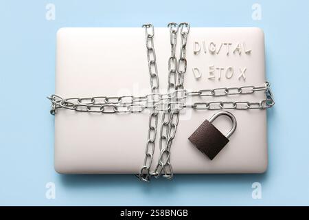 Modern laptop tied with chain, padlock and text DIGITAL DETOX on color background Stock Photo