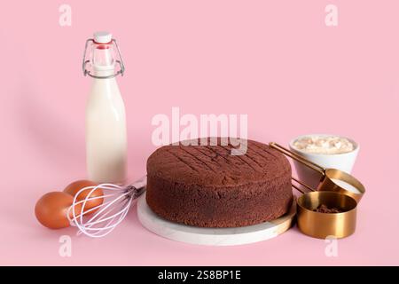 Delicious chocolate sponge cake with ingredients and kitchen utensils on pink background Stock Photo