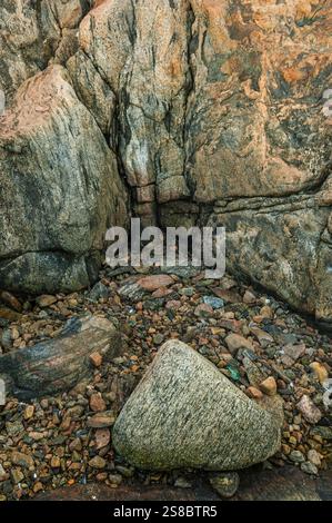 This coastal view captures a rocky shoreline featuring various stones and pebbles scattered on the beach. The soft sunlight illuminates the textured s Stock Photo