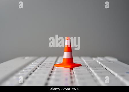 A miniature traffic cone on a laptop keyboard. Website maintenance, downtime, or technical difficulties concept. Stock Photo