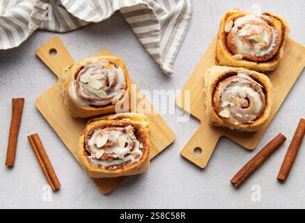 Freshly baked cinnamon rolls, drizzled with icing and sprinkled with almonds, sit on wooden cutting boards, ready to be enjoyed Stock Photo