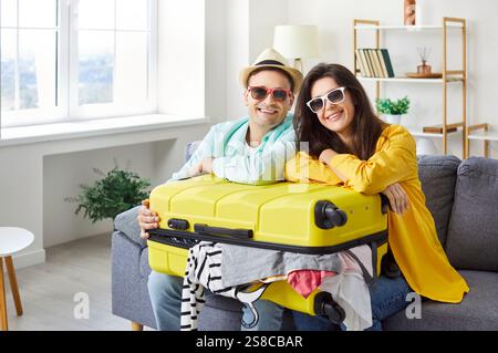 Happy couple in sunglasses with suitcase sitting on sofa Stock Photo