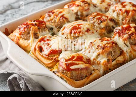 Homemade baked sliders stuffed with meatballs, topped with tomato sauce and grated cheese close-up in a baking dish on a table. horizontal Stock Photo