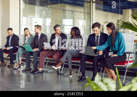 Diverse group of business people sitting in row collaborating and communicating during work meeting. Stock Photo