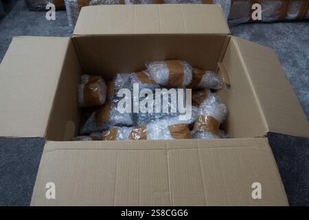 A cardboard box is filled with bubble-wrapped items. The box is open, and the contents are visible.  The box is sitting on a gray floor. Stock Photo