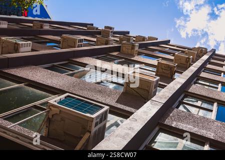 An older style high rise office building with multiple single room external air conditioners attached to the exterior of the building Stock Photo