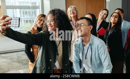 A diverse team of successful coworkers happily taking a selfie together at work during a daytime event, showcasing positivity and teamwork in a modern Stock Photo