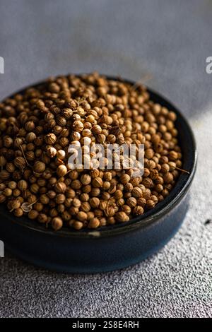 A close-up view of raw coriander seeds in a dark bowl, placed on a textured concrete table Stock Photo