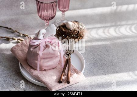 An artistic Easter table arrangement featuring a bunny-themed pink cloth wrap, elegantly tied, accompanied by unique pink glasses and a delicate willo Stock Photo
