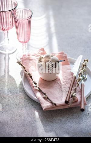 An elegant and festive Easter table setting in soft pastel hues. The focus is a decorative egg centerpiece surrounded by blooming willow twigs on a pi Stock Photo