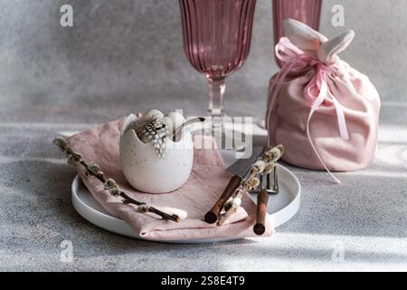 Beautifully arranged Easter table setting featuring a cracked eggshell vase with feathers, surrounded by pink elements and spring decorations. Soft li Stock Photo