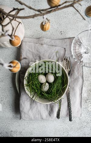 Top view of a beautifully arranged Easter table featuring a bowl filled with grass and speckled eggs, surrounded by vintage silverware and a branch wi Stock Photo