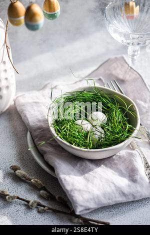 A fresh Easter setting featuring painted eggs tucked delicately within lush green grass, arranged in a ceramic bowl, complemented by subtle spring acc Stock Photo