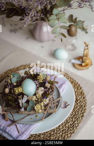 Top view of an Easter table setting featuring a plate with a rustic nest of twigs and naturally dyed eggs, surrounded by floral decorations and subtle Stock Photo