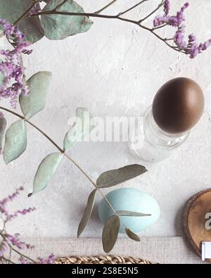 Top view of a delicate Easter table setup featuring naturally dyed eggs in soft blue and shades of brown, complemented by subtle floral decorations an Stock Photo