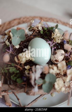 A close-up view of a detailed Easter nest containing naturally dyed eggs amidst a variety of flowers and plants, elegantly arranged on a serene tablet Stock Photo