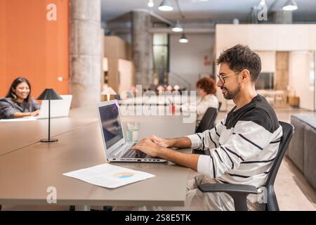 Diverse coworkers engaged in teamwork at a contemporary open space office Individuals working independently on laptops, fostering creativity and produ Stock Photo