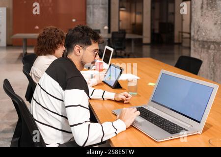 Two coworkers collaborate in a modern office, using laptops and tablets to enhance productivity The workspace emphasizes teamwork, technology, and inn Stock Photo