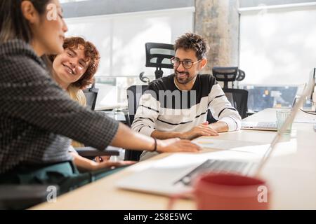 A group of coworkers engaged in a collaborative discussion at a modern office Smiling and communicating, they foster teamwork and creativity in a frie Stock Photo
