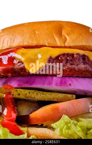 Close-up of a juicy cheeseburger layered with melted cheddar cheese, red onion, pickles, tomato, lettuce and ketchup served on a toasted golden bun Stock Photo