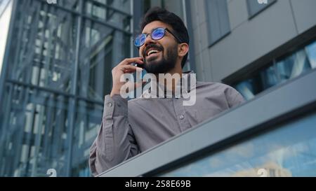 Joyful Indian man talking mobile phone on office terrace outdoors happy smiling Arabian businessman employer ceo executive talk smartphone in city Stock Photo