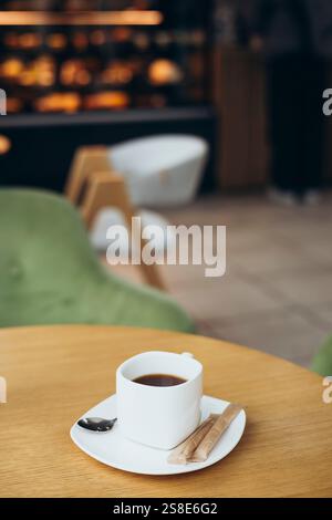 A steaming cup of coffee sits on a wooden table in a cozy cafe setting The background shows blurred chairs and decor, adding to the warm and inviting Stock Photo