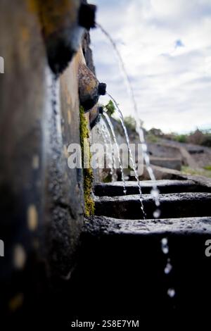 Close-up view captures water flowing through an old, moss-covered stone water channel, symbolizing traditional irrigation methods in El Tanque, Teneri Stock Photo