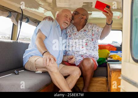 Elderly gay couple sharing a tender moment while camping inside their off-road vehicle. One man kisses the other's forehead as they create memories, w Stock Photo
