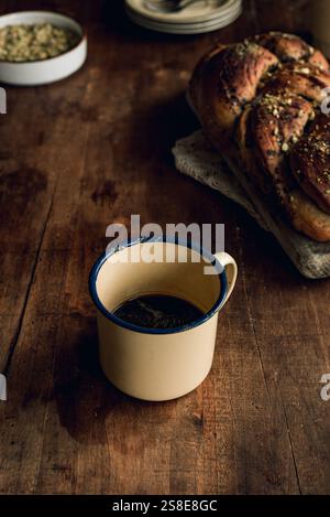 Top view of a freshly baked Bakbah bread garnished with pistachio, alongside a vintage tin cup filled with black coffee, presented on a rustic wooden Stock Photo