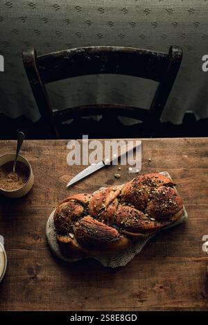 Top view of a freshly baked chocolate and pistachio babka bread, placed on a rustic wooden table beside a bowl of sugar and a knife. The image capture Stock Photo