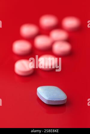 A vivid image showcasing a blue pill prominently in focus with several pink pills in the background, all arranged on a bright red surface, creating a Stock Photo