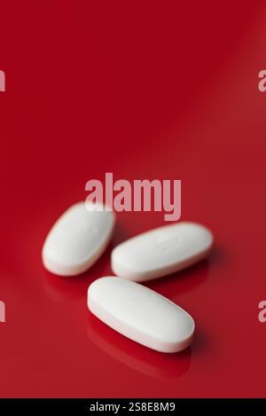 A minimalist image featuring three oblong white tablets, subtly embossed, isolated against a deep red background with a soft focus setting. Stock Photo