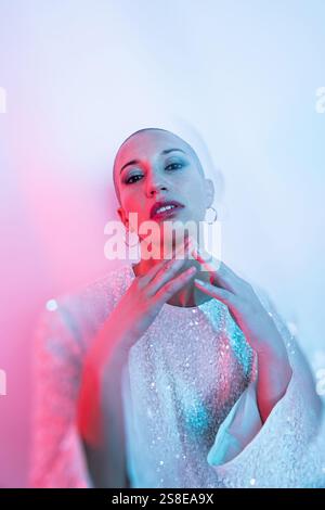 Middle-aged woman with shaved head in stylish pose, adorned with intricate attire. Artistic lighting creates a dreamy ambiance, highlighting her confi Stock Photo