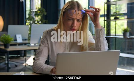 Caucasian businesswoman girl office manager confused business woman working laptop eyestrain problem take off glasses blurry vision bad eyesight Stock Photo