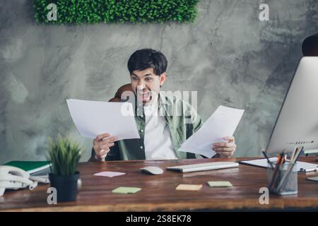 Young businessman in casual office setting enthusiastically reviewing documents with modern workspace interior design Stock Photo