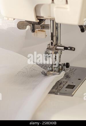 Detailed close-up of a sewing machine in action, stitching a delicate white sheer fabric. The needle and thread are precisely sewing the material, sho Stock Photo