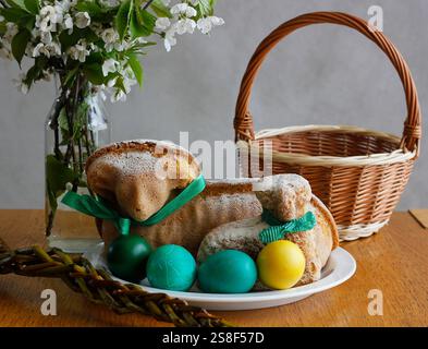 Easter still life containing two lamb cakes, four painted eggs, a wicker basket, an Easter whip and and blooming cherry twigs in a vase Stock Photo