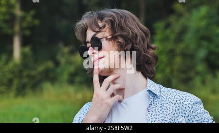 Contemplative young man in sunglasses ponders his post graduation future with a hand on his chin Stock Photo
