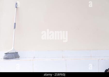 A clean, minimalistic scene featuring a broom leaning against a plain wall. The floor is tiled and spotless, emphasizing cleanliness and simplicity. Stock Photo