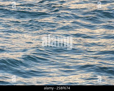 Ocean scene with soft waves rolling onto the shore bathed in warm evening light, capturing the essence of a peaceful summer day Stock Photo