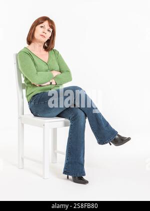 Casual Concern. A contemplative look and body language from a casually dressed mature woman sitting on a chair, isolated on a white background. Stock Photo