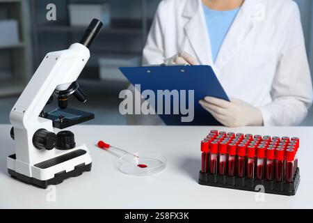 Laboratory testing. Doctor working at table indoors, focus on microscope and blood samples Stock Photo