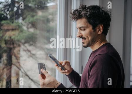 Young handsome middle eastern man using phone and credit card and smiling. card e-banking online shop e-commerce Stock Photo