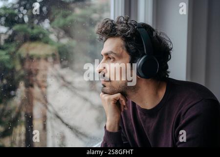 Good looking middle eastern man with on-ear headphones listening to music and relaxing near a window. Stock Photo