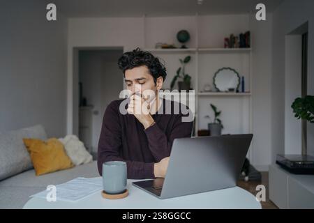 Young stressed looking handsome middle eastern man using computer and being overwhelmed by work. Stock Photo