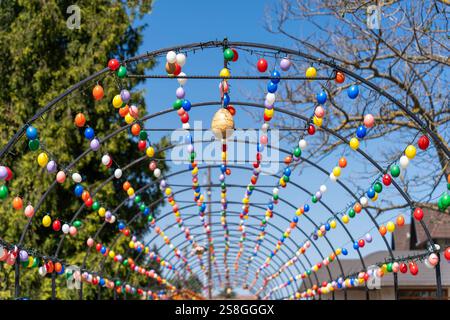 A festive metal archway decorated with strings of colorful Easter eggs, creating a cheerful holiday display under a bright blue sky. Stock Photo
