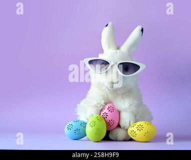 Easter bunny in sunglassis with colorful easter eggs on a violet background Stock Photo